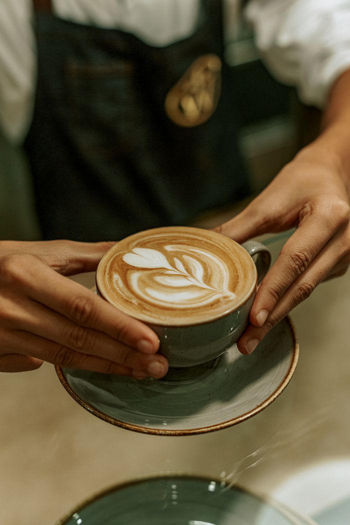ours-journey Close-up of a barista serving a latte with intricate leaf art at a café in Baku, Azerbaijan.
