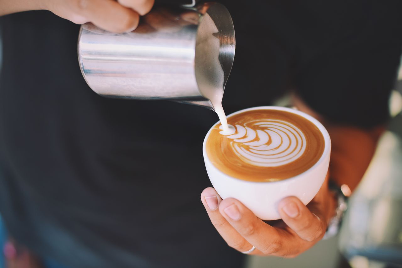 gallery-1 Captivating image of a barista pouring milk art into a cappuccino cup, showcasing latte art skills.