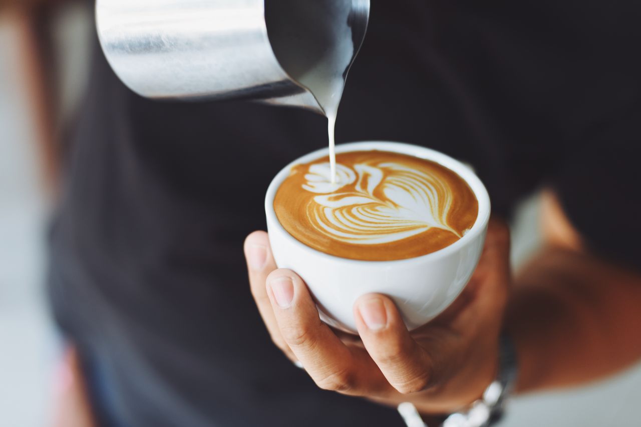 services-02 Close-up of a barista pouring milk to create latte art in a coffee cup.