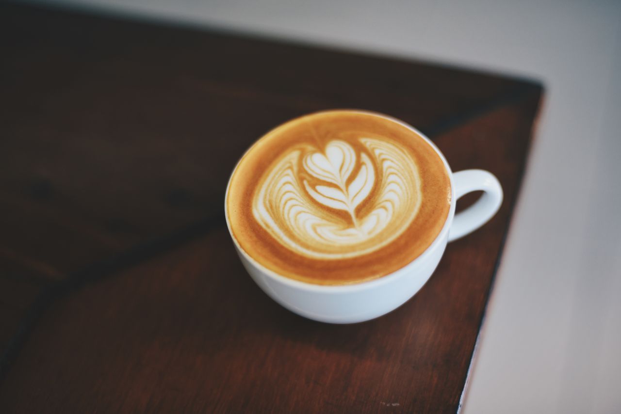 services-01 A beautifully crafted latte with intricate foam art in a white porcelain mug on a dark wooden table.