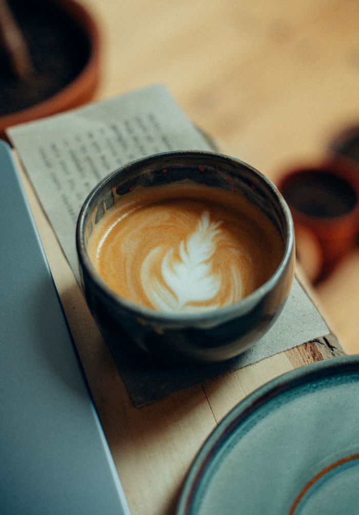 gallery-2 A beautifully crafted latte with latte art in a rustic ceramic cup on a wooden table.