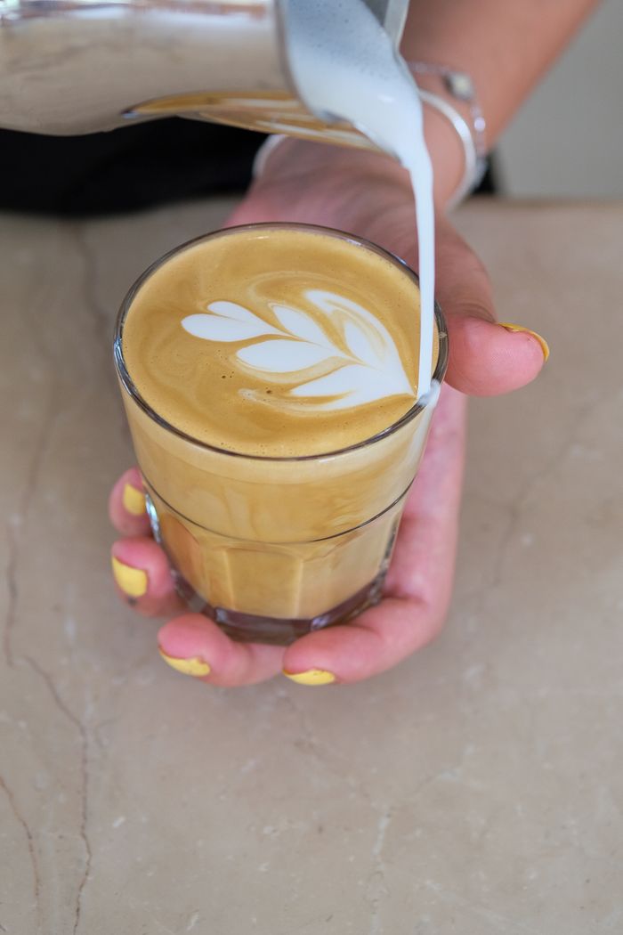 our-experience Close-up of a barista creating latte art in a glass cup at a café.