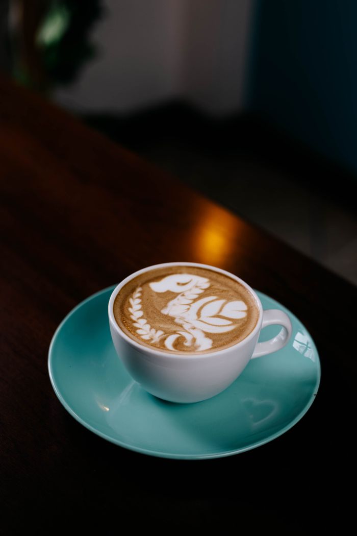 gallery-3 Close-up of a beautifully crafted latte with latte art in a turquoise cup on a wooden table.