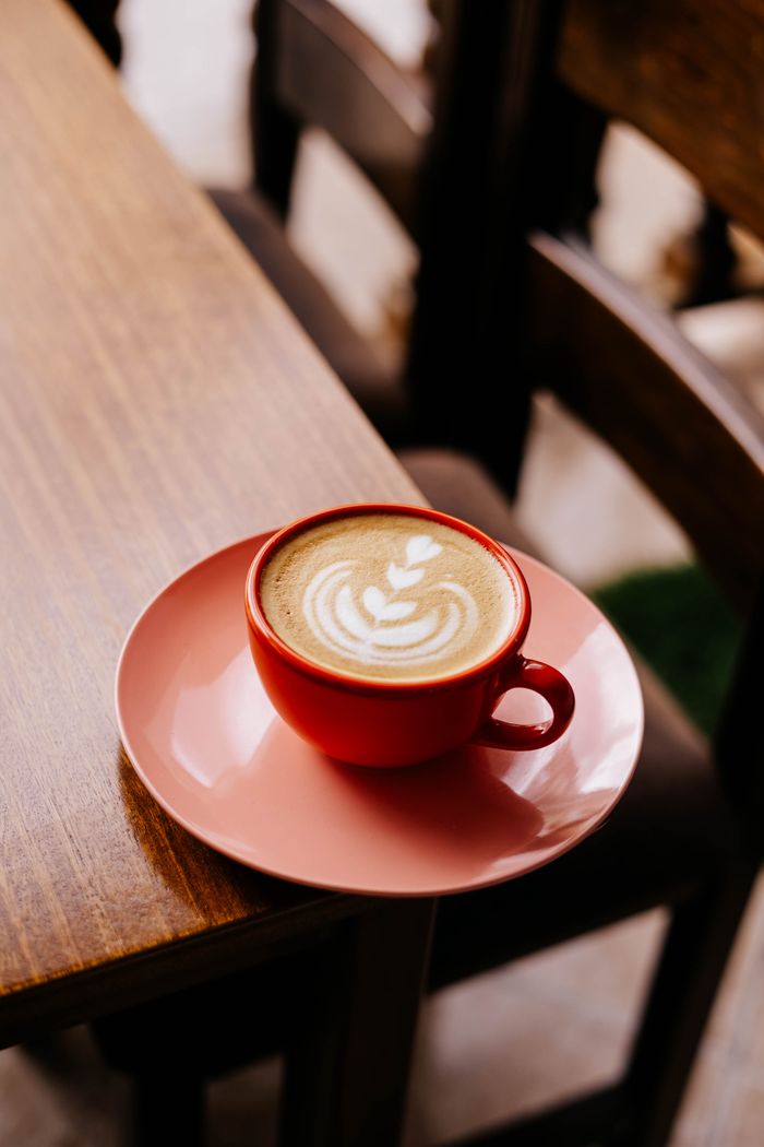 gallery-4 A red cup with latte art sits on a table in a cozy cafe setting, inviting warmth.