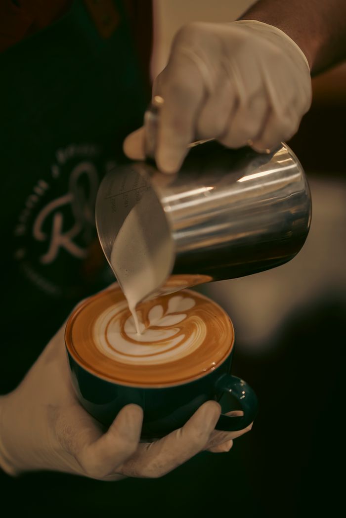 services-03 Barista pouring intricate latte art into a cup of coffee in a cozy cafe setting.