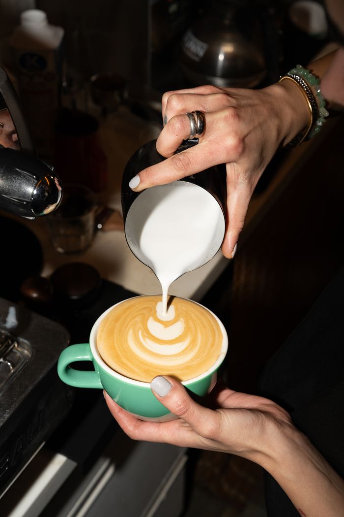 Close-up of barista pouring milk to create latte art in a green cup.