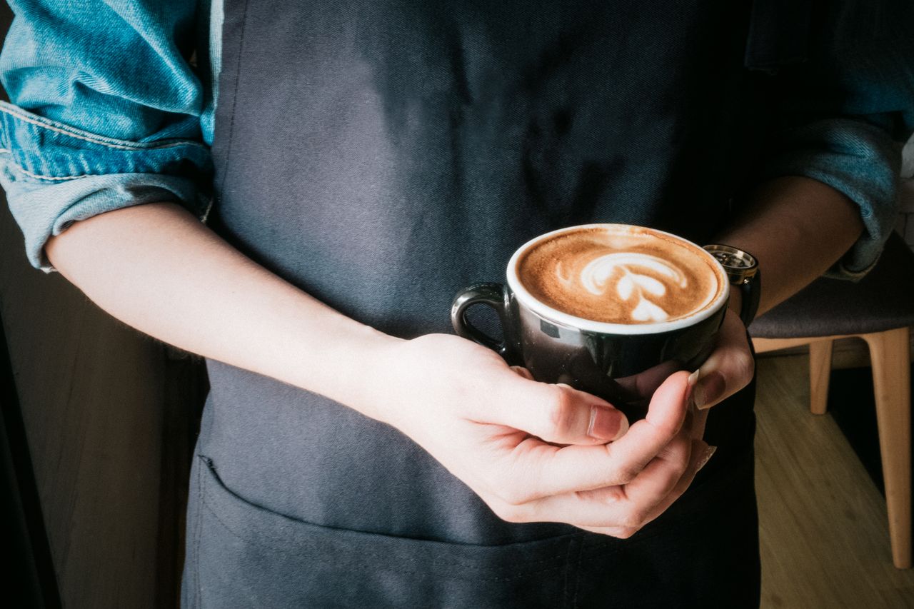 services-01 A barista holds a coffee cup with beautiful latte art in a cozy café setting.
