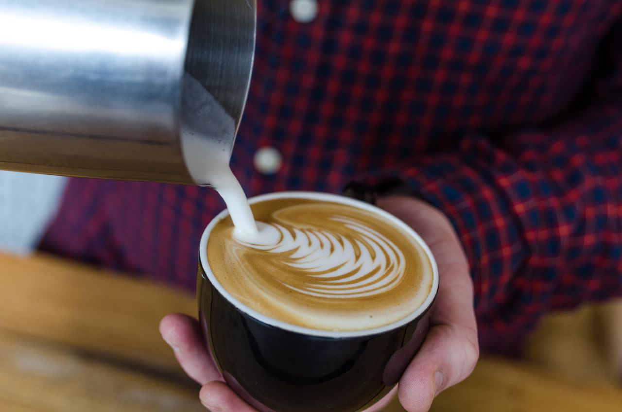 A barista skillfully pouring latte art into a cup of coffee, creating a beautiful design.