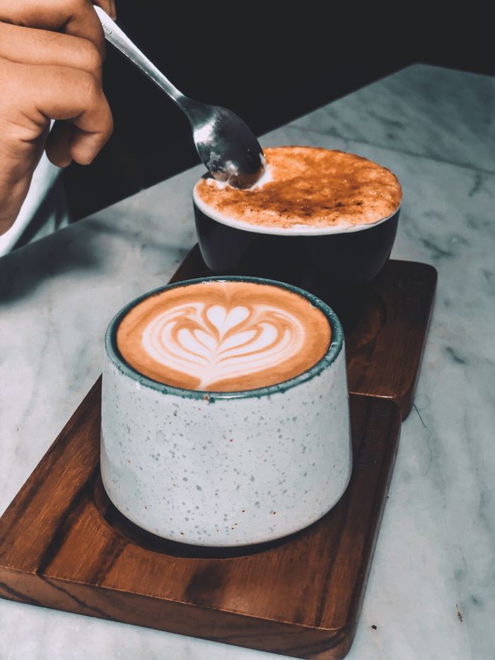 about-img Two coffee cups with latte art on a wooden board, captured in a cozy setting.