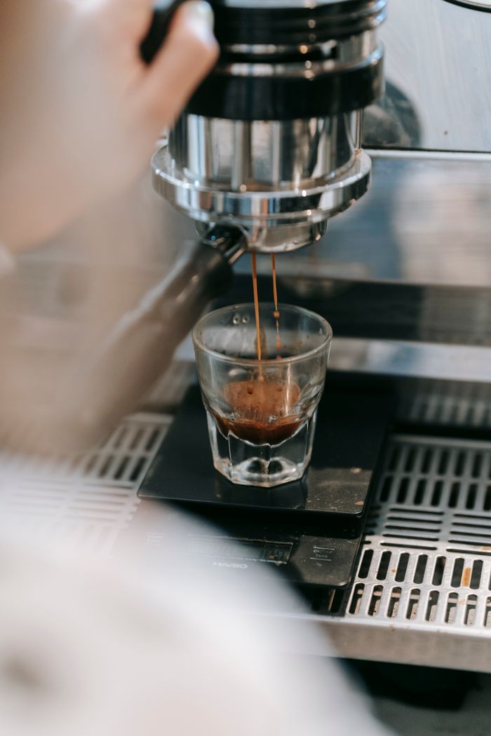 services-02 Close-up view of espresso shot being poured into a glass under a coffee machine.